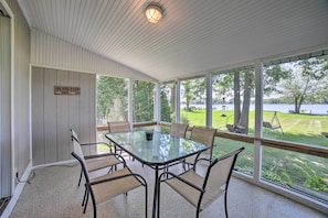 A covered patio with a glass table and chairs, a sign reading "ON OUR PATIO", and a view of a grassy area and trees.