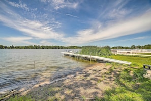 A lakeside view with a wooden dock extending into the water, surrounded by grassy areas and trees.