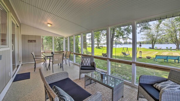A covered patio with wicker furniture, large windows, and a view of a lake. - Rome City Waterfront Oasis w/ Beach & Dock! (Rome City)