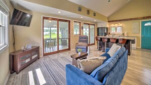 A spacious living area with a blue sofa, a flat-screen TV mounted on the wall, and a ceiling fan. - Rome City Waterfront Oasis w/ Beach & Dock! (Rome City)