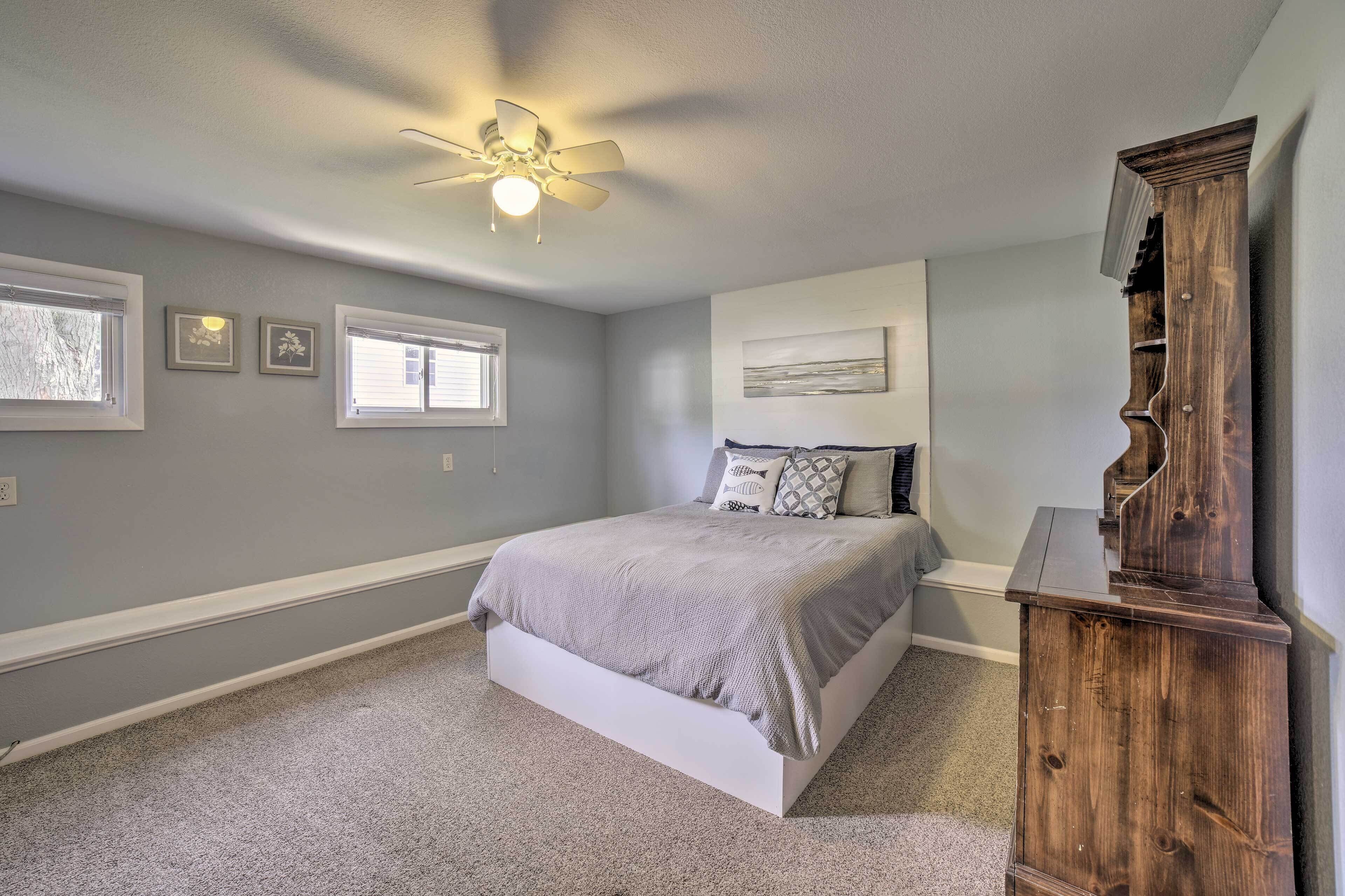 A bedroom with a bed, a ceiling fan, a dresser, and framed pictures on the wall.