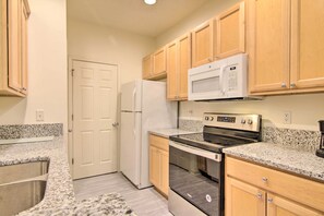 A kitchen with granite countertops, a white refrigerator, a microwave, an oven, and wooden cabinets. - Porch & Community Perks: Walkable Lewes Condo (Lewes)