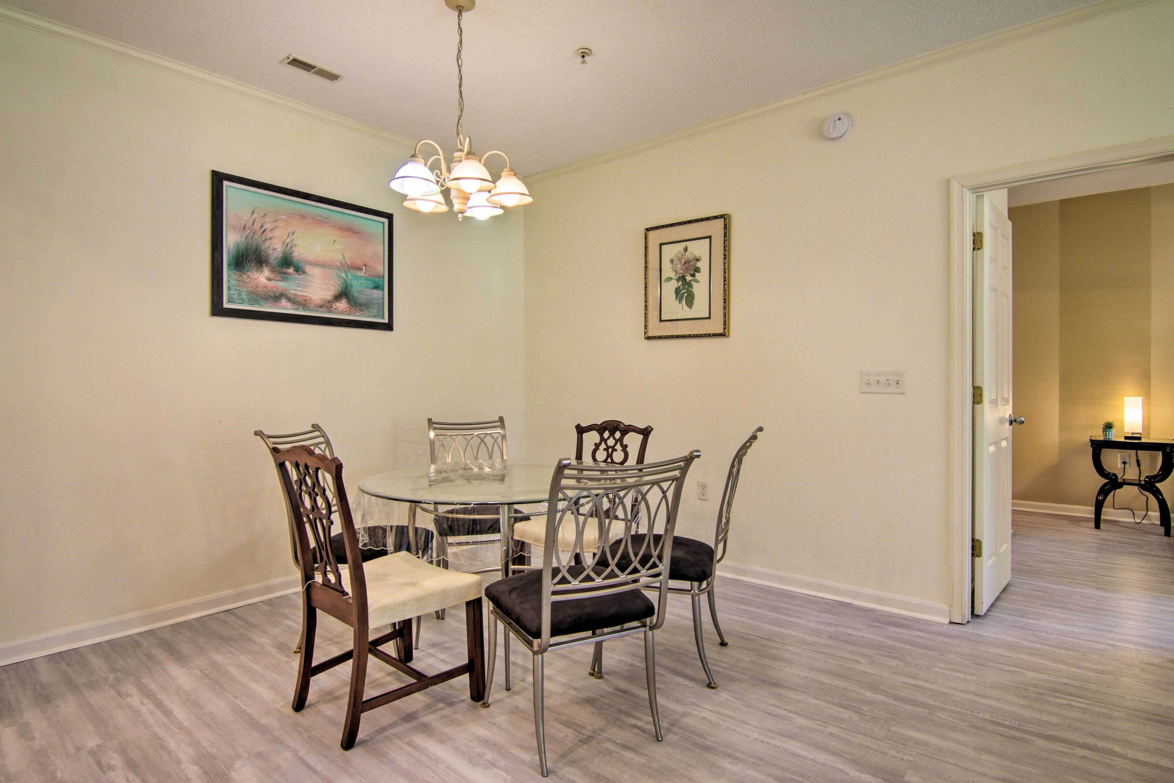 A dining area with a round table, four chairs, and a chandelier.