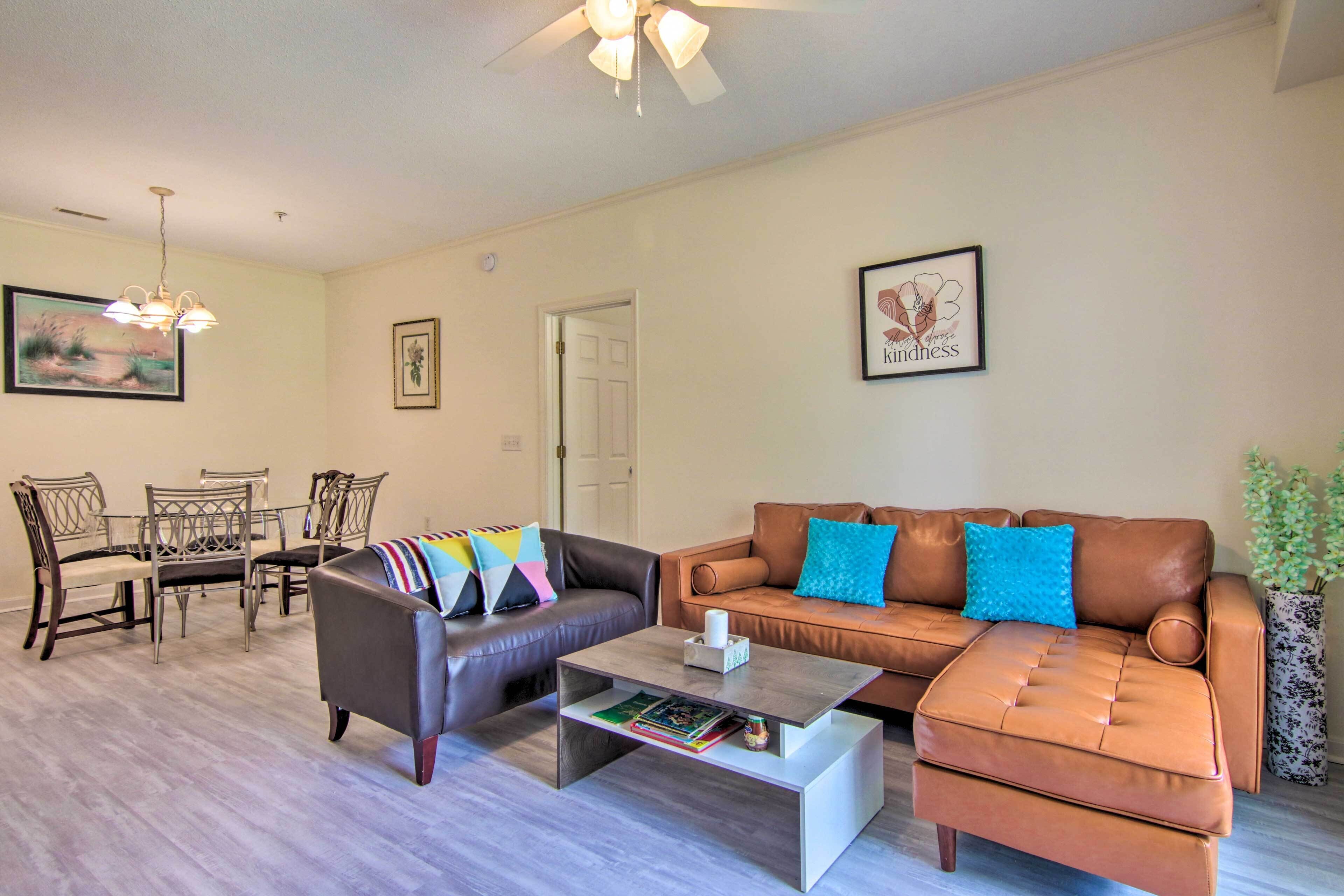 A living room with a brown leather sofa, a coffee table, a dining table with chairs, and a ceiling fan.