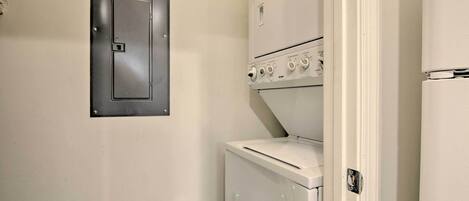 A compact laundry room with a washer and dryer, a metal utility door, and a thermostat on the dryer.