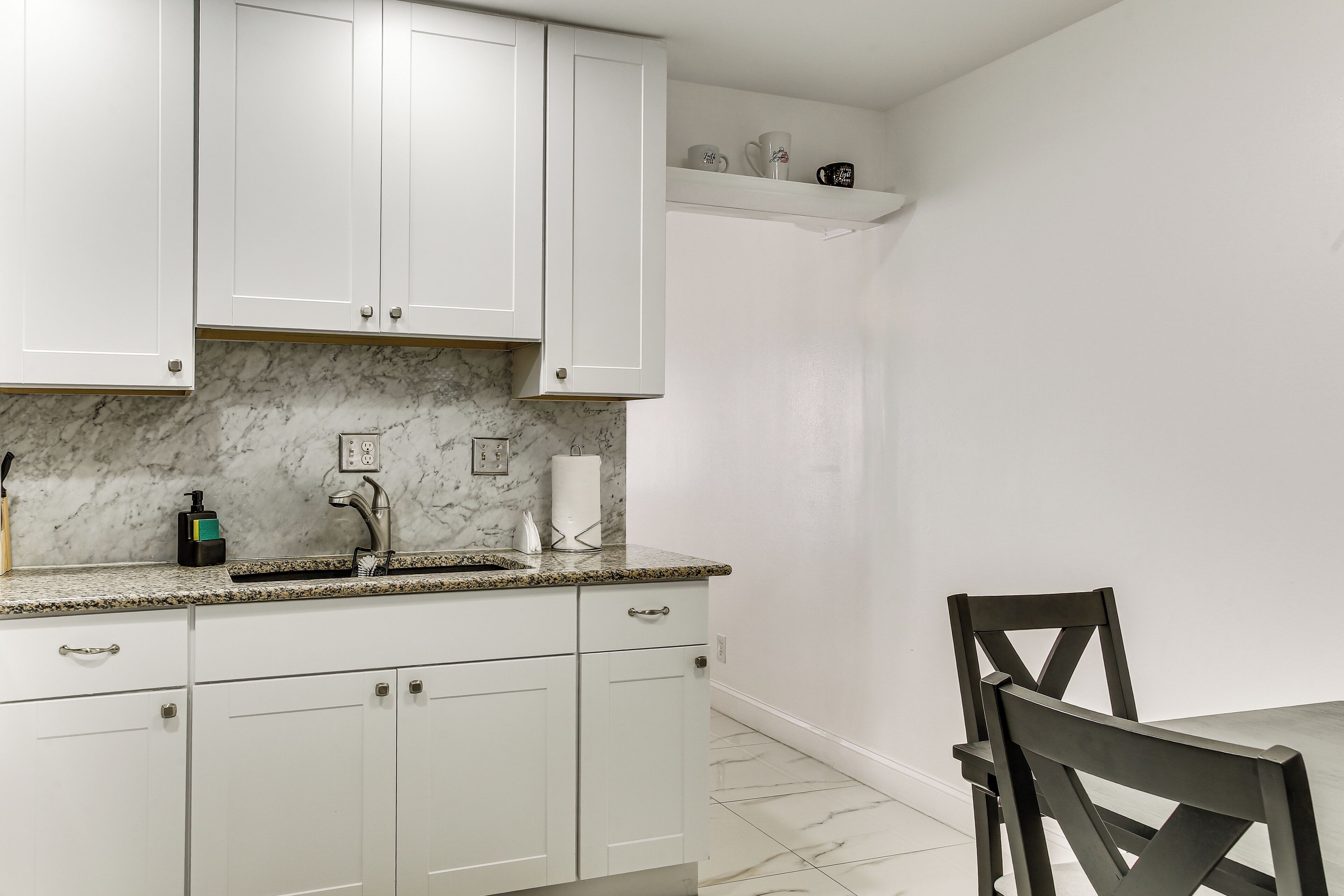 A kitchen with white cabinets, a marble countertop, a sink, and a chair.