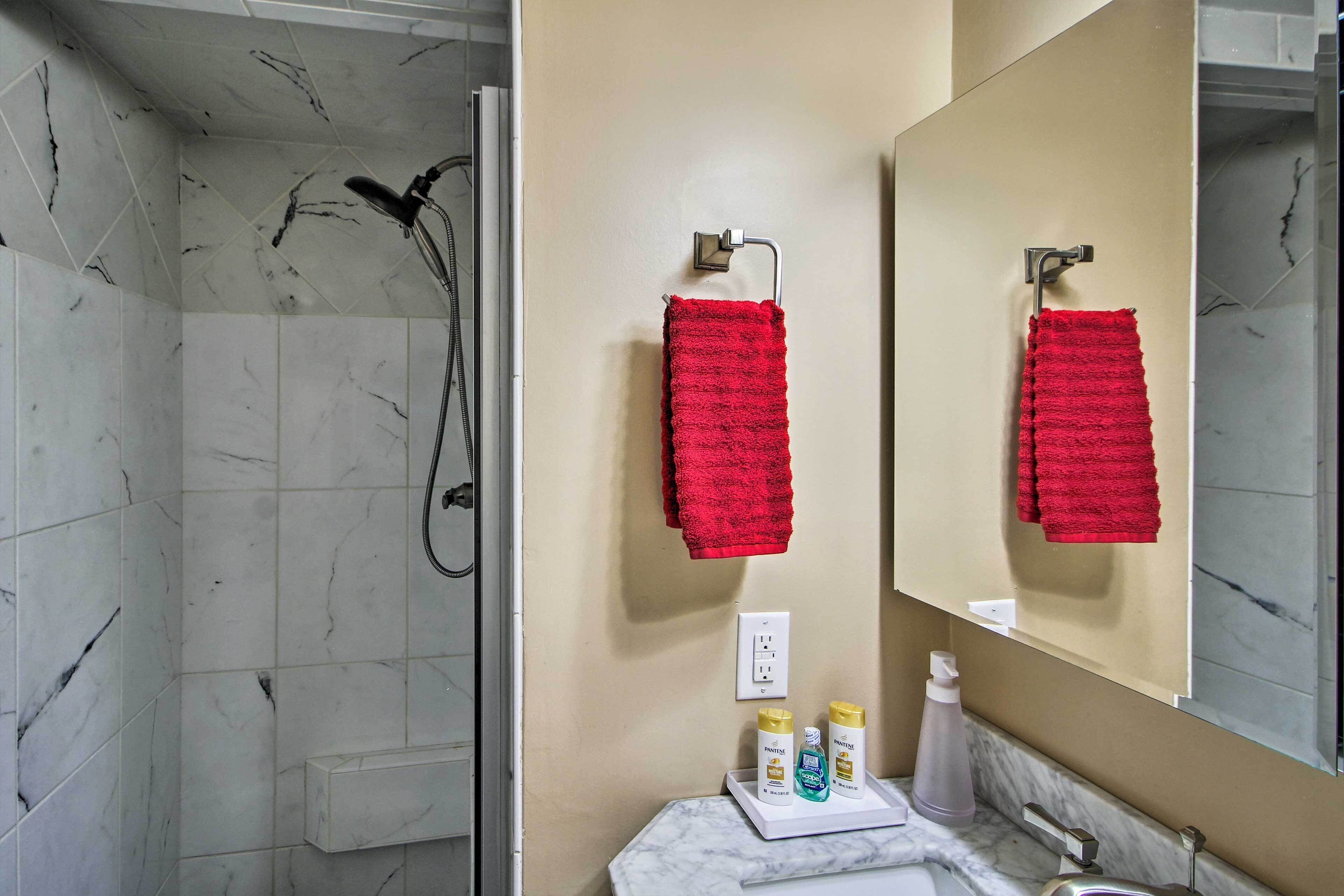 A bathroom with a shower, a sink, a mirror, and red towels.