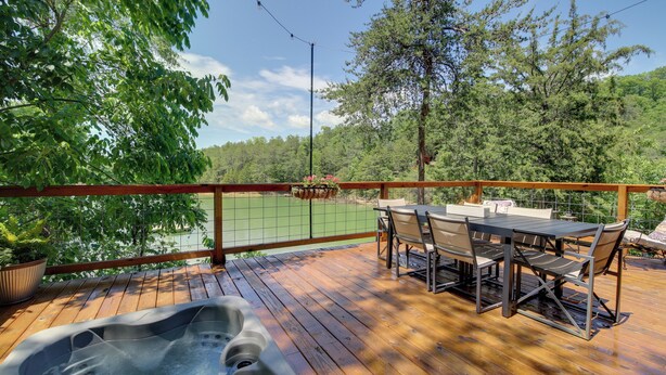 A wooden deck with a hot tub, outdoor seating, and a view of a forested area. - Lakefront Cabin in the Smoky Mountains (Sevierville)
