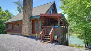 A log cabin with a stone chimney, wooden porch, and a view of a lake. - Lakefront Cabin in the Smoky Mountains (Sevierville)