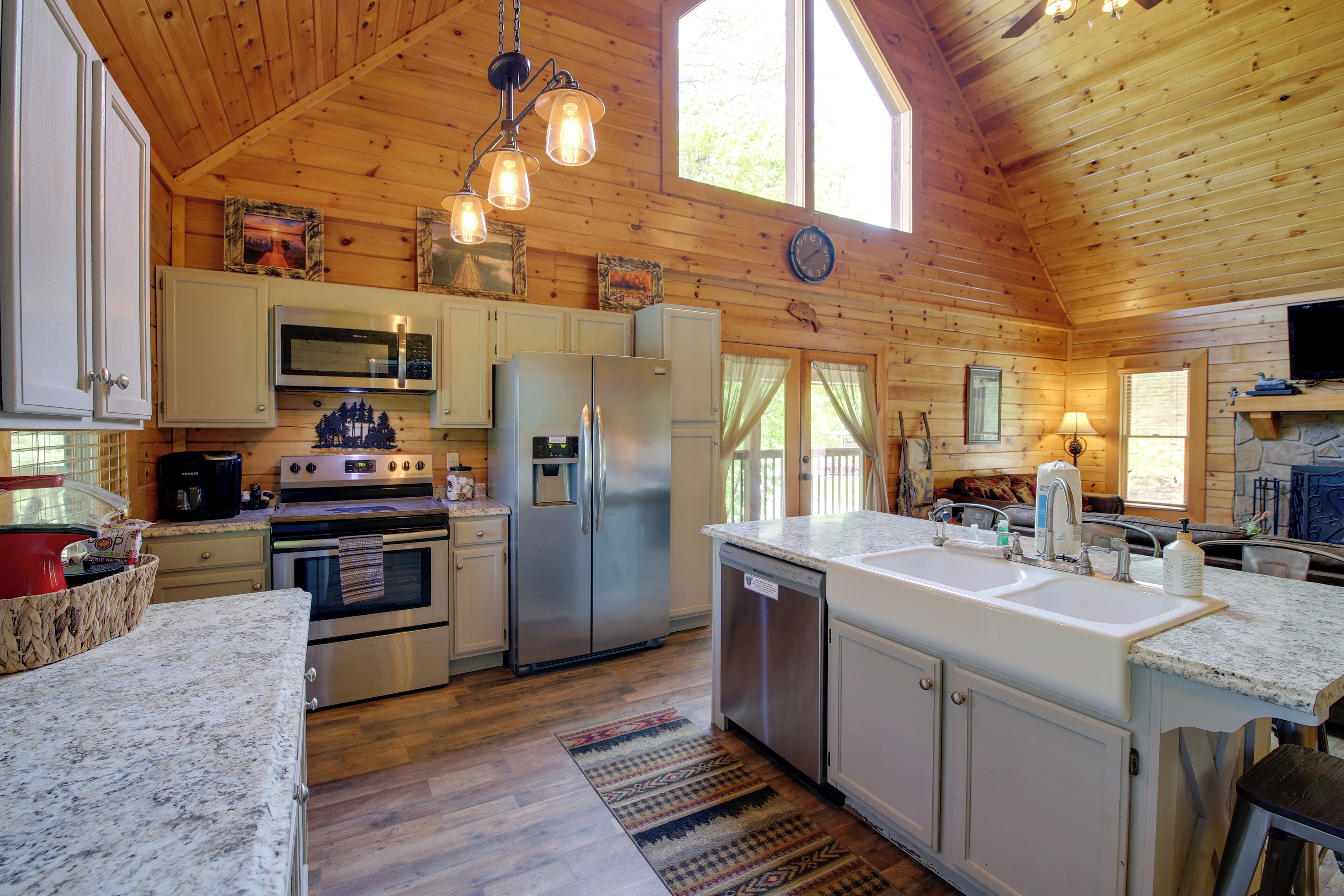 A spacious kitchen with wooden walls, a large island with a sink, stainless steel appliances, and a clock on the wall.
