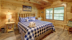 A wooden cabin bedroom with a bed, nightstands, a window, and a painting on the wall. - Lakefront Cabin in the Smoky Mountains (Sevierville)