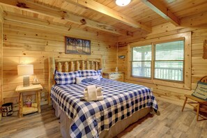 Ein Schlafzimmer einer Holzhütte mit einem Bett, Nachttischen, einem Fenster und einem Bild an der Wand.