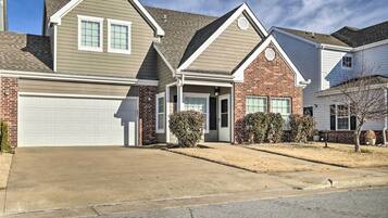 A residential house with a garage, brick exterior, and a small front yard with shrubs.