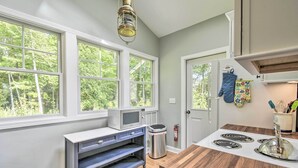 Eine Küche mit Mikrowelle, Herd und Mülleimer. Fenster bieten Blick auf Bäume.