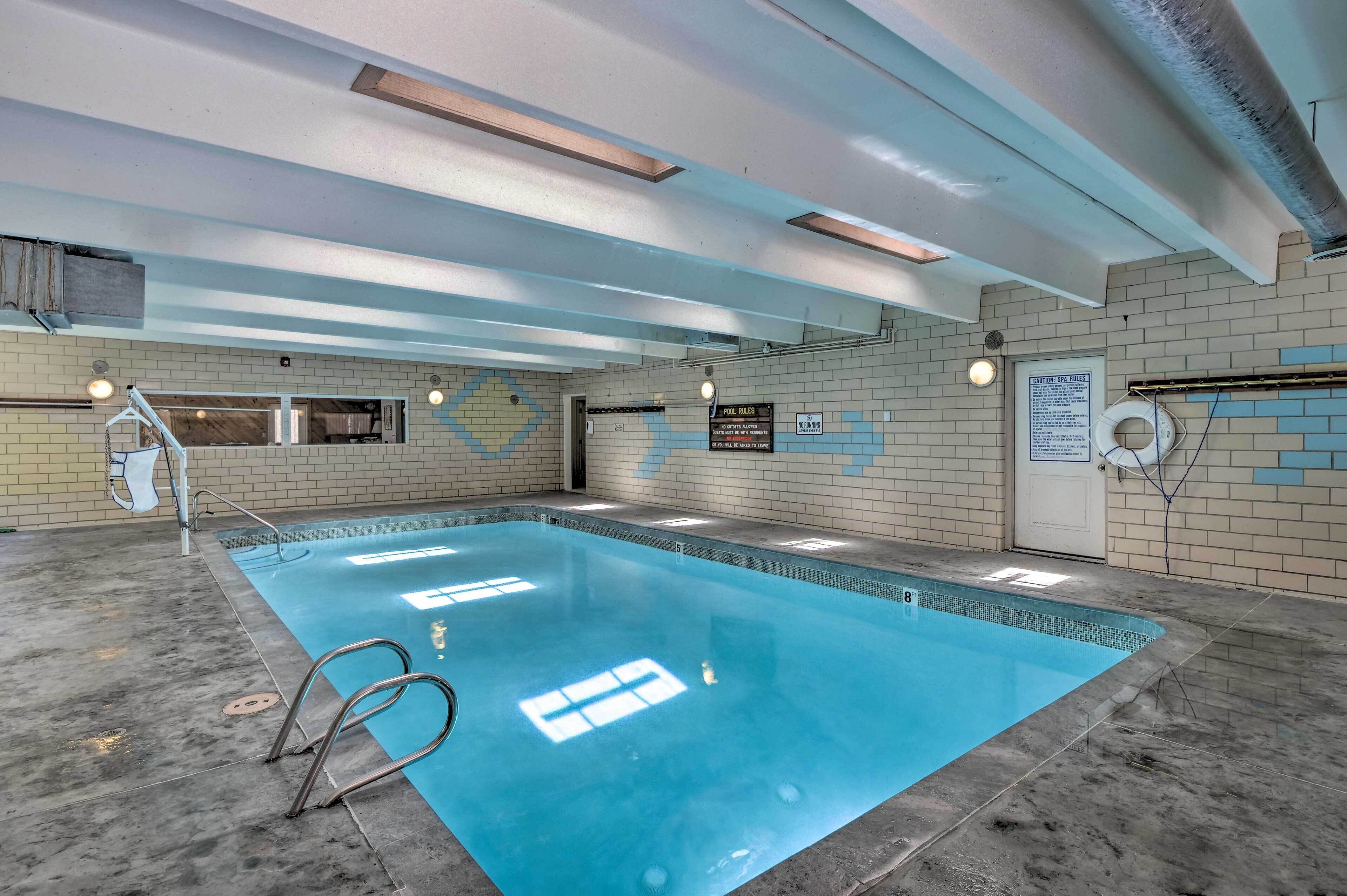 En indendørs swimmingpool med klart vand, fliserede vægge og et loft med synlige bjælker.