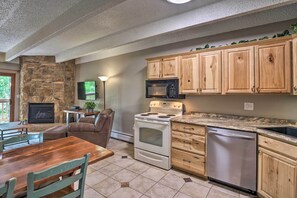 A kitchen with a stone fireplace, wooden cabinets, a white stove, a microwave, and a dishwasher. - Frisco Condo 2 Blocks to Main St: Year-round Fun! (Frisco)