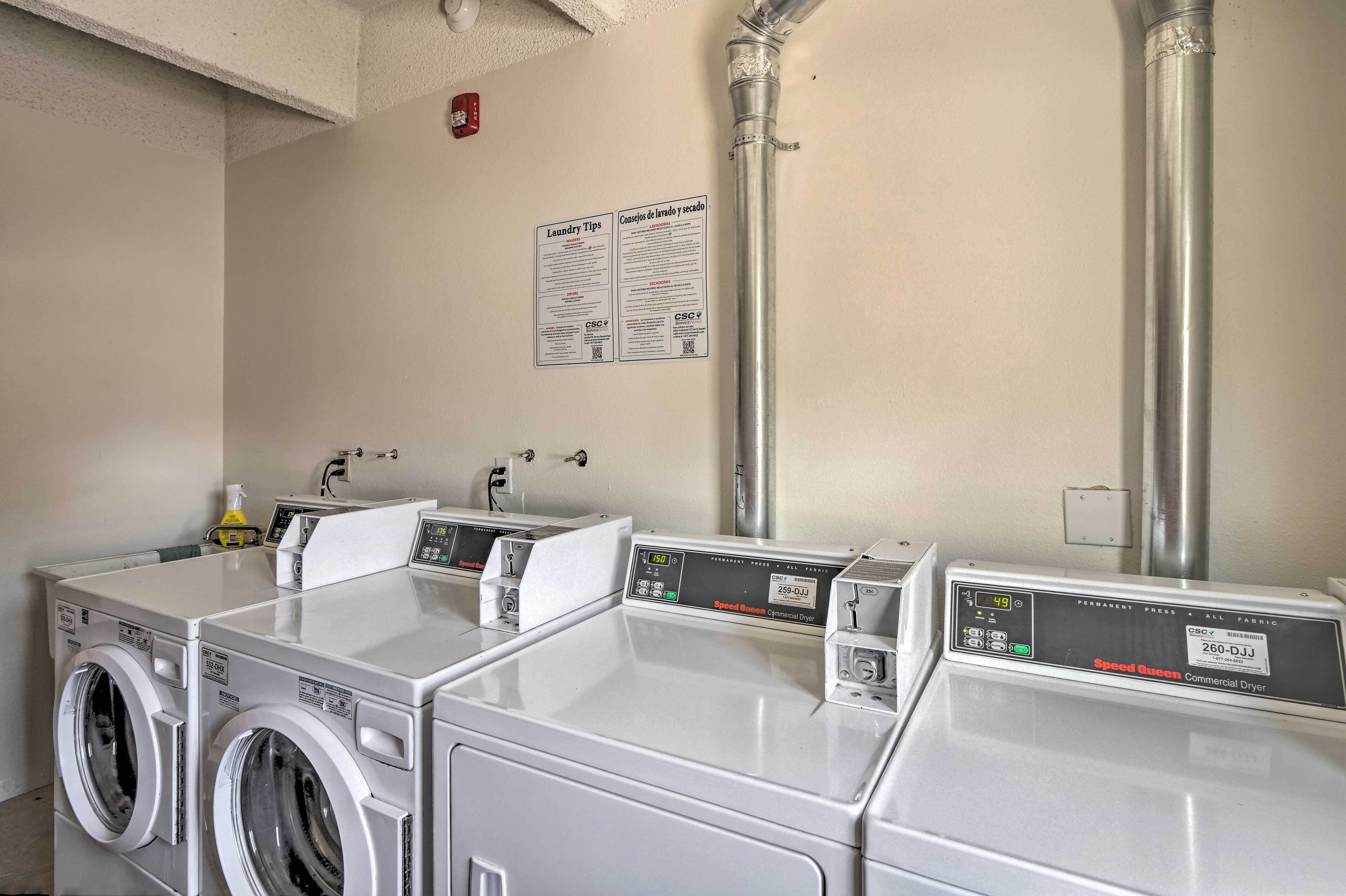 Une buanderie équipée de plusieurs machines à laver et de plusieurs sèche-linge, d’un panneau explicatif fixé au mur et d’une tuyauterie visible.