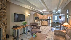 A spacious living room with a stone wall, a flat-screen TV, a leather recliner, a coffee table, and a dining area with wooden chairs and a table. - Frisco Condo 2 Blocks to Main St: Year-round Fun! (Frisco)