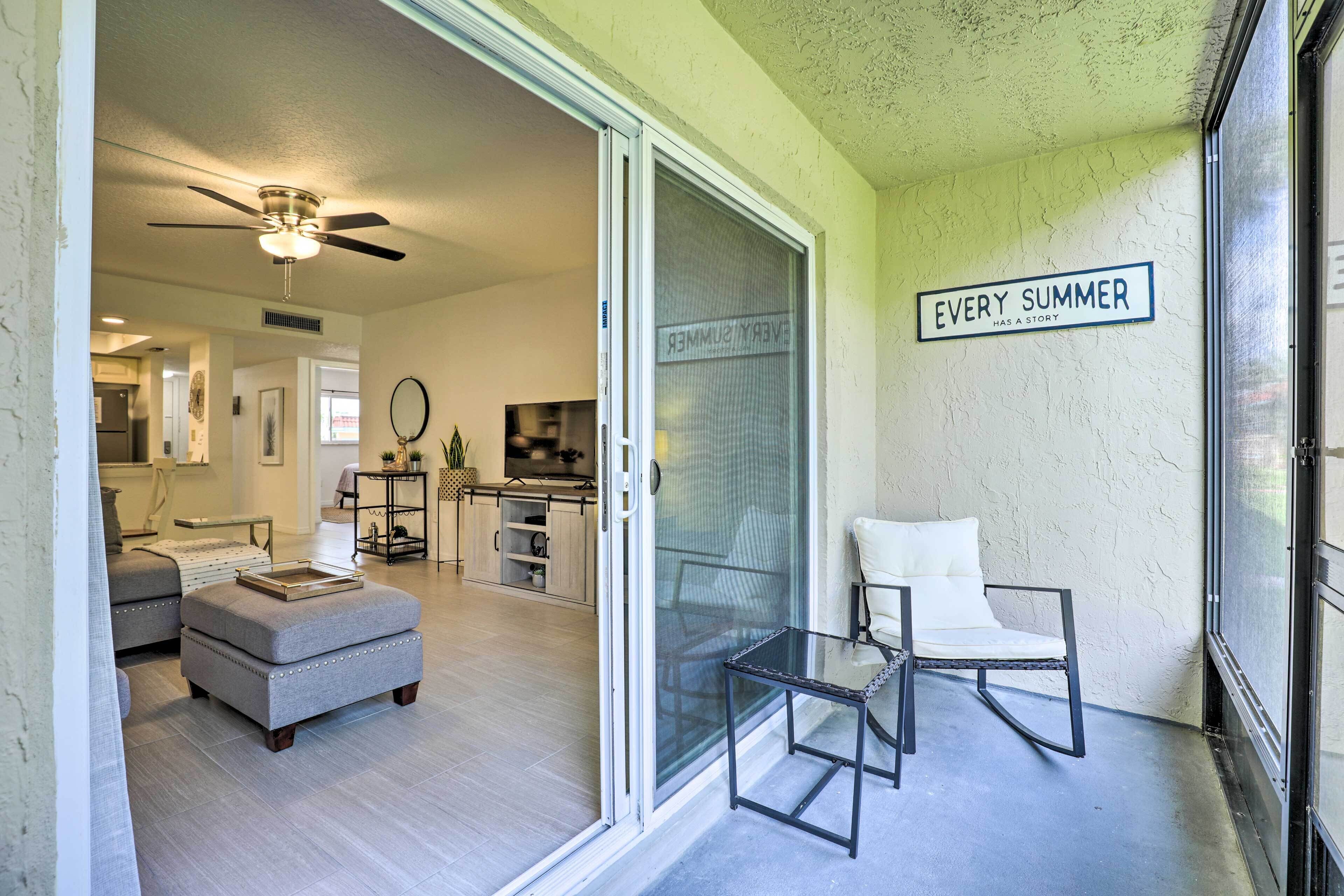 Un salon moderne avec des meubles recouverts d’un tissu gris, une porte en verre donnant sur un balcon et un ventilateur de plafond.