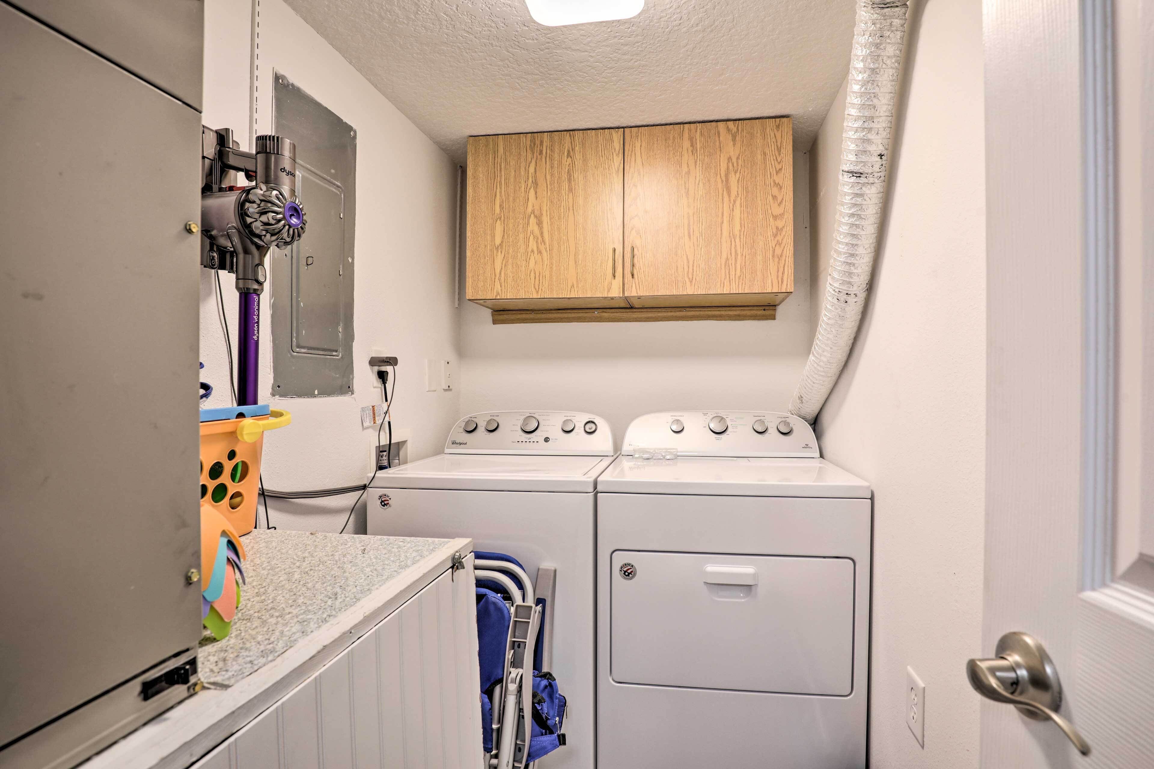 A compact laundry area with a washing machine and dryer, a wooden cabinet above, and a small countertop with a basket.