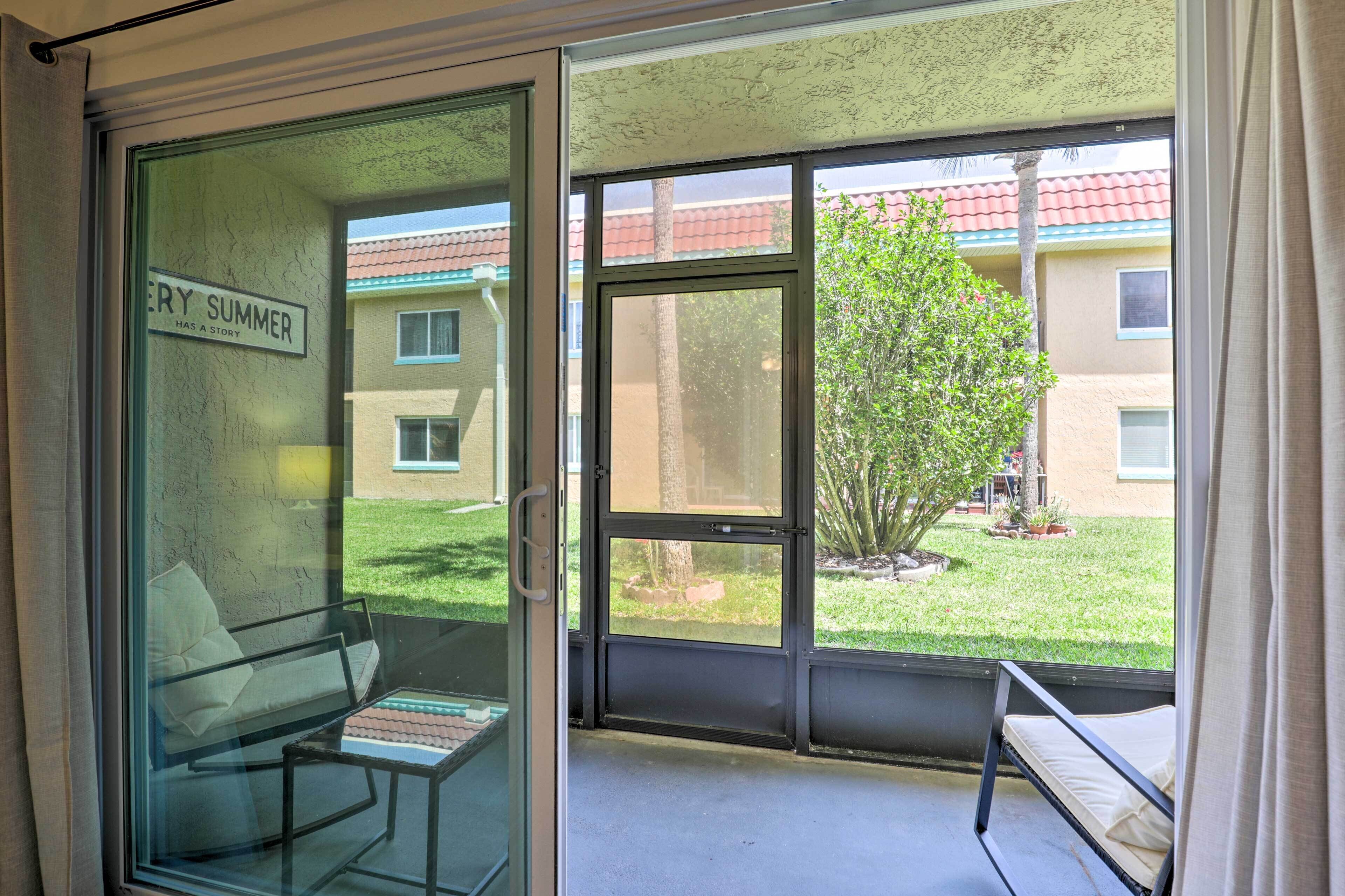 A room with a sliding glass door leading to a balcony. The room has a bed and a chair.