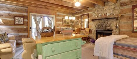A cozy log cabin room with a stone fireplace, a green dresser, a bed with a striped blanket, and a wicker basket on the dresser.