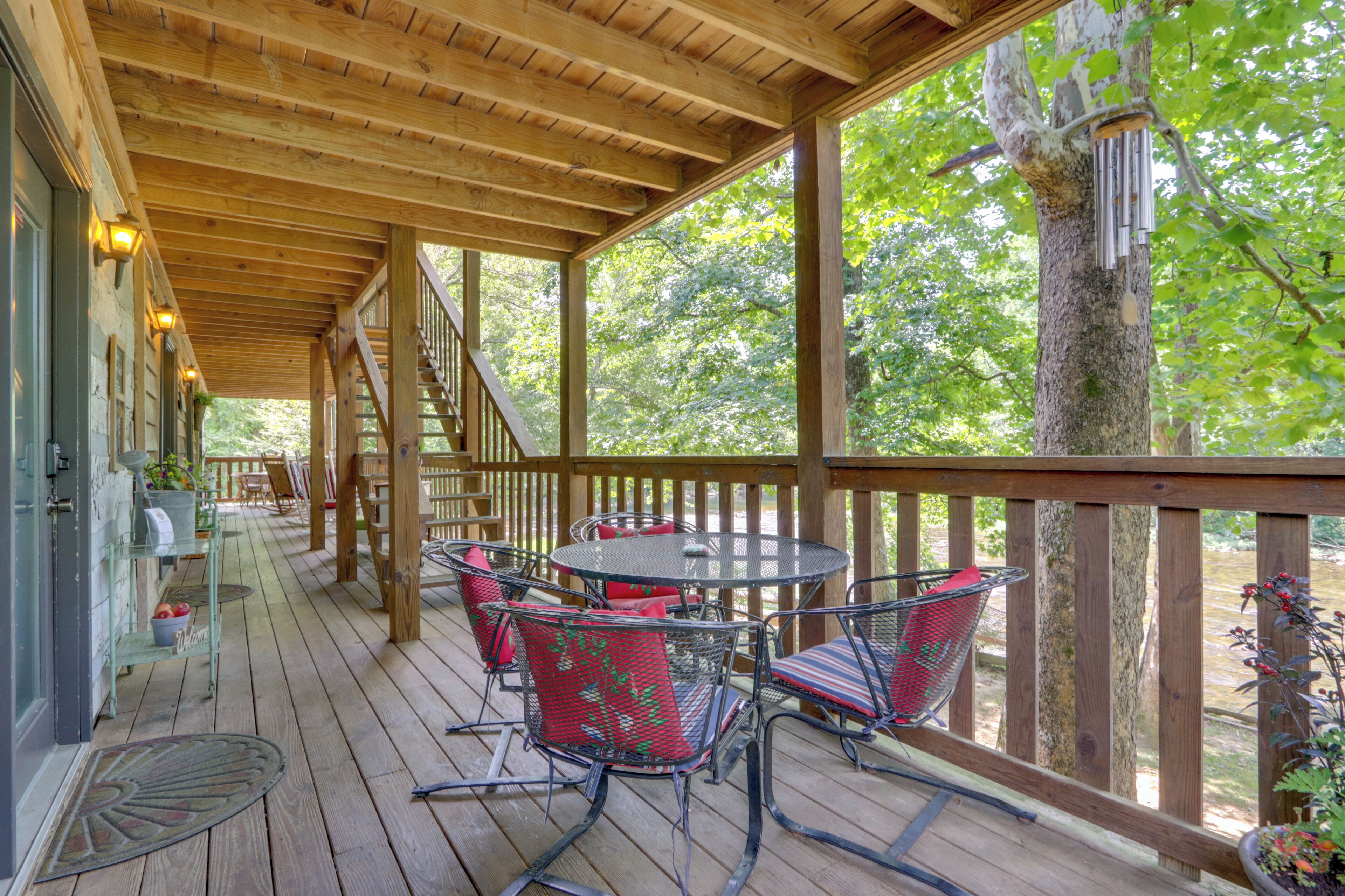 A covered outdoor deck with a wooden railing, a round table with chairs, and a staircase leading to an upper level.