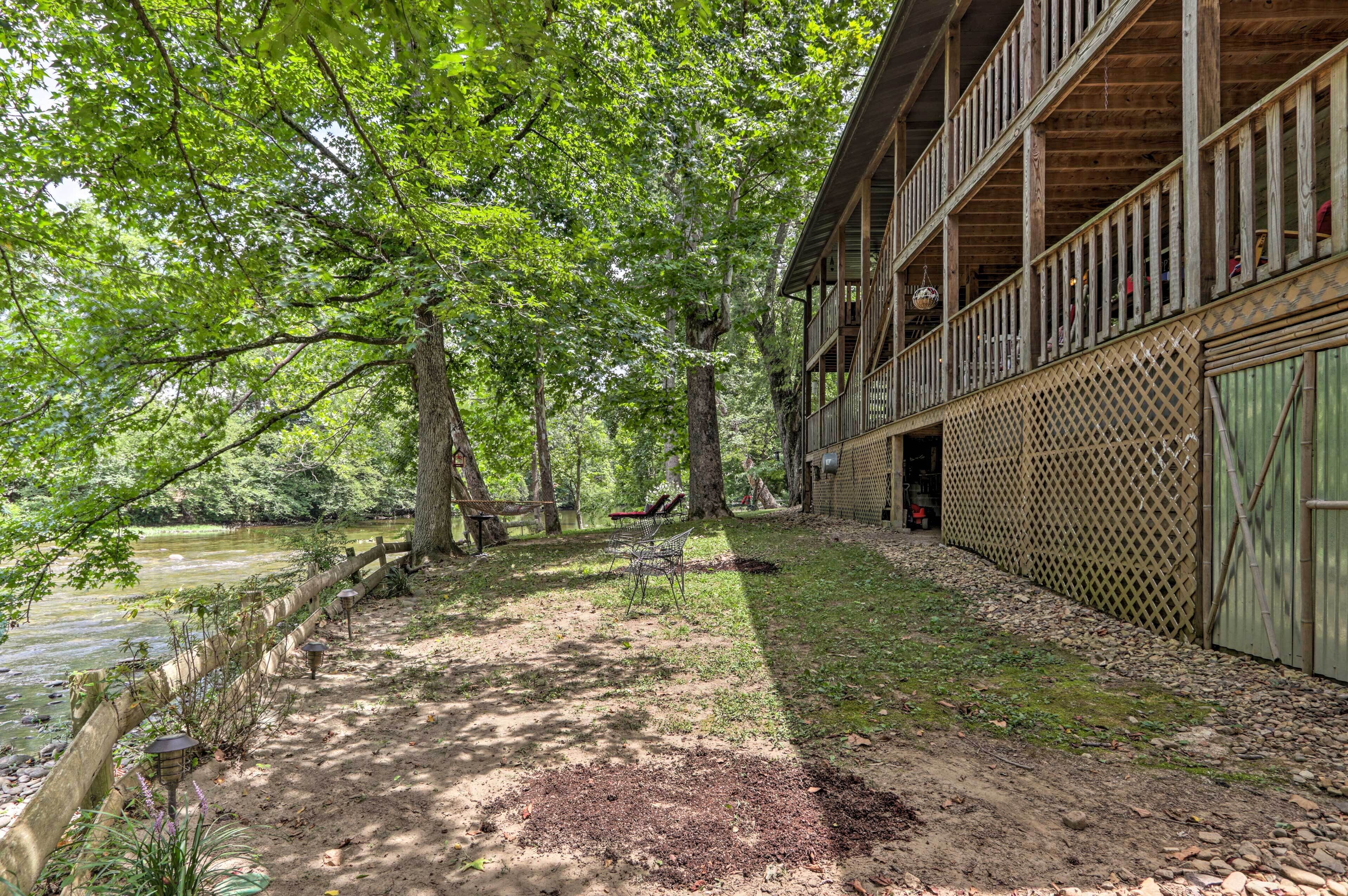 A wooden cabin with a balcony overlooking a pond, surrounded by trees.