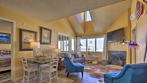 A spacious living room with a fireplace, a dining area with a table and chairs, and a large window offering a view of the outdoors. - Cozy Ski-in/ski-out Granby Condo w/ Balcony! (Granby)