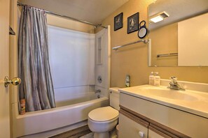 Bathroom features a bathtub, shower curtain, toilet, and sink with a mirror.