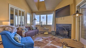 A cozy living room with a fireplace, large windows, and a sofa with a fur throw. - Cozy Ski-in/ski-out Granby Condo w/ Balcony! (Granby)