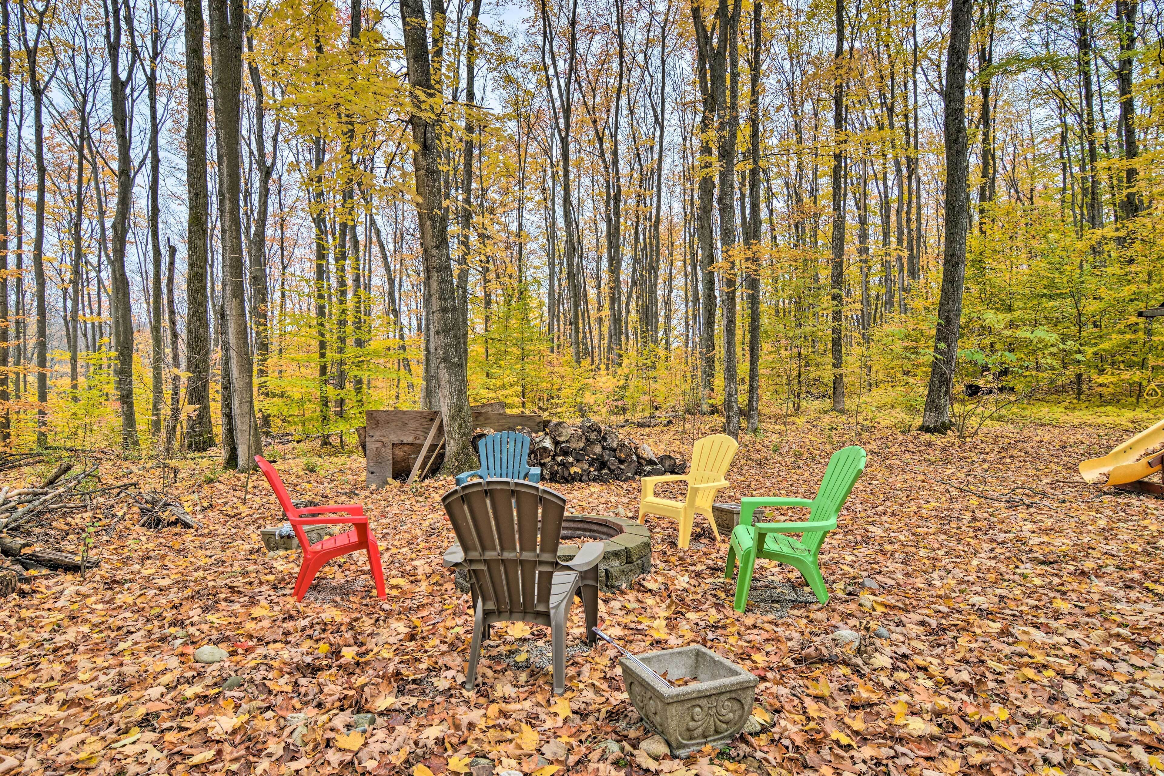 Une clairière dans la forêt, avec un foyer, plusieurs fauteuils Adirondack et une pile de bois de chauffage.