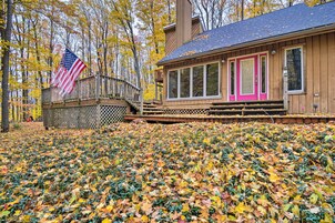 A wooden cabin with a pink door, a deck, and an American flag.