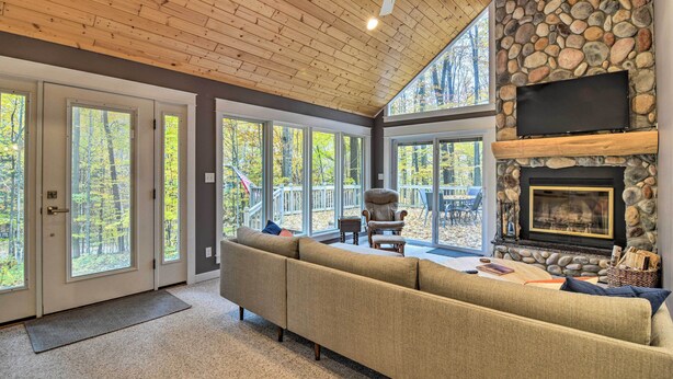 A spacious living room with a stone fireplace, a large sofa, and a ceiling fan. - Family Escape - Near Little Traverse Wheelway (Harbor Springs)