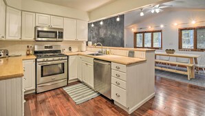 A kitchen with white cabinets, stainless steel appliances, a wooden countertop, and a dining area with a table and chairs. - Family Escape - Near Little Traverse Wheelway (Harbor Springs)