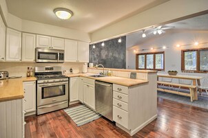Una cocina con armarios blancos, electrodomésticos de acero inoxidable, encimera de madera y un comedor con mesa y sillas.