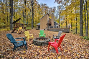 A cabin with a deck, surrounded by autumn leaves, and a fire pit with chairs.