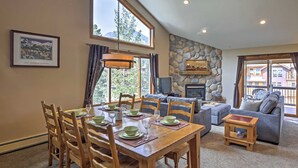 A dining area with a wooden table set for six, a stone fireplace, and a view of the outdoors through large windows. - Half-mi to Copper Mtn Slopes: Frisco Unit w/ Loft (Frisco)