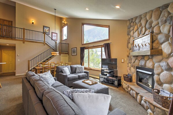 A spacious living room with a stone fireplace, a large window, and a staircase leading to an upper level. - Half-mi to Copper Mtn Slopes: Frisco Unit w/ Loft (Frisco)