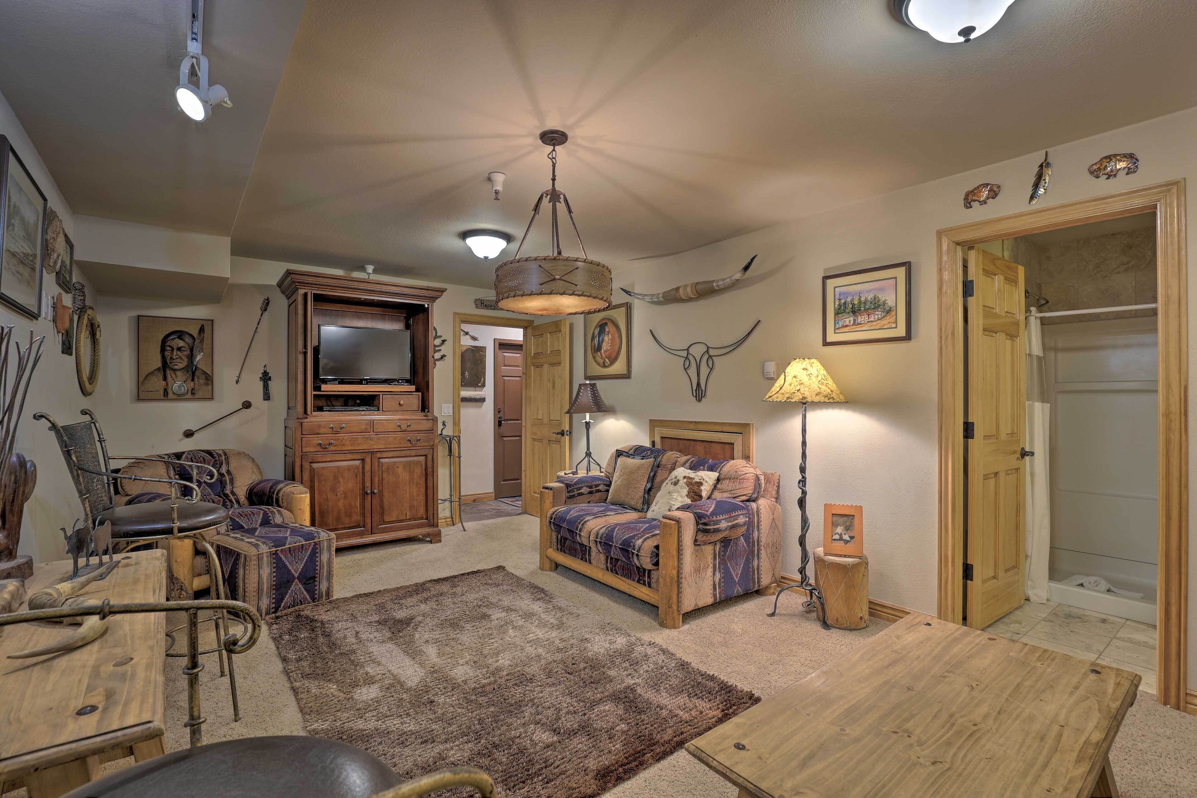 Un salon chaleureux avec un canapé en bois, une table basse et une cheminée. On y trouve également un téléviseur et une lampe fixée au mur.
