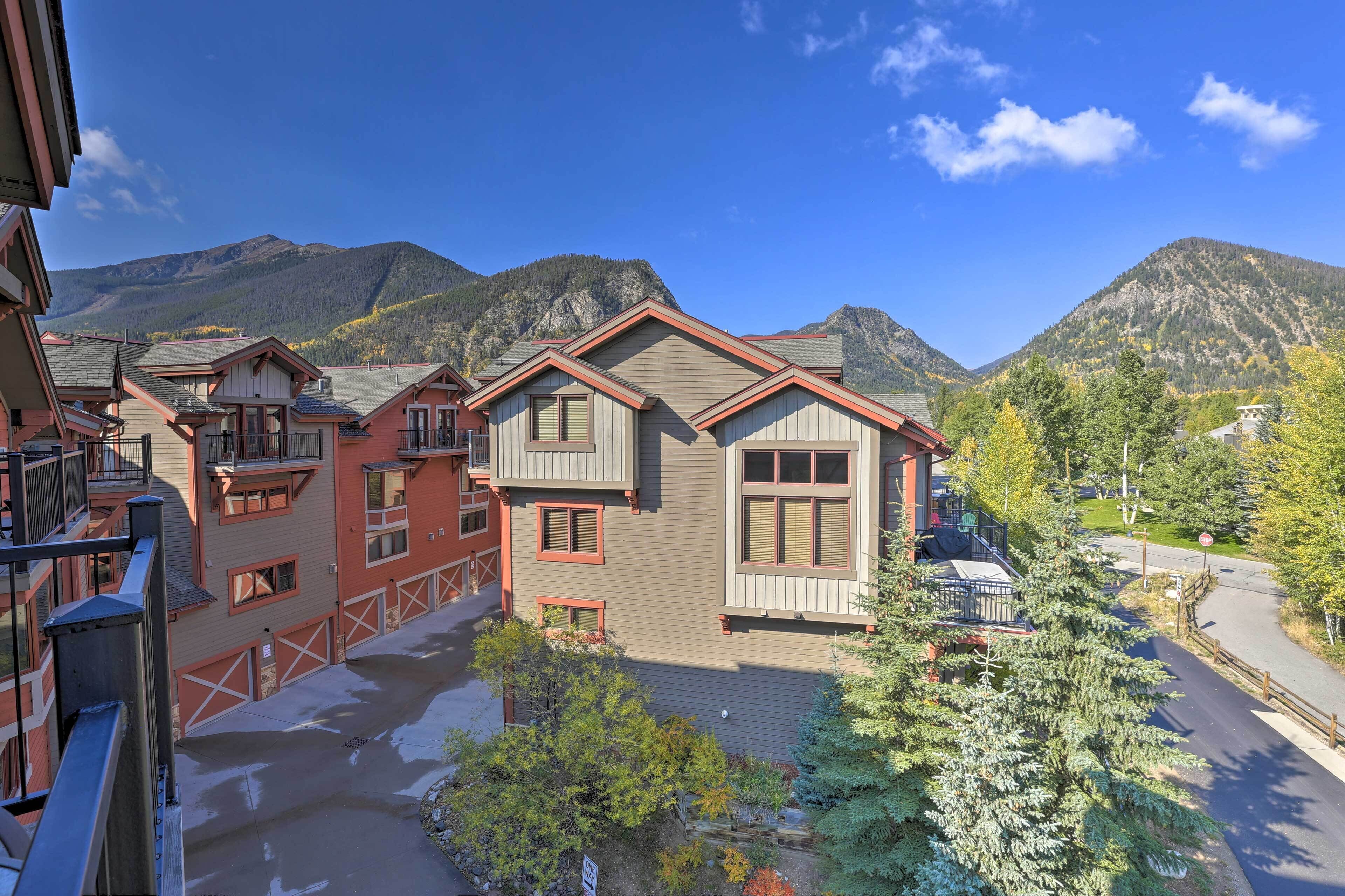 A multi-story building with a red and beige facade, multiple balconies, and a view of mountains in the background.