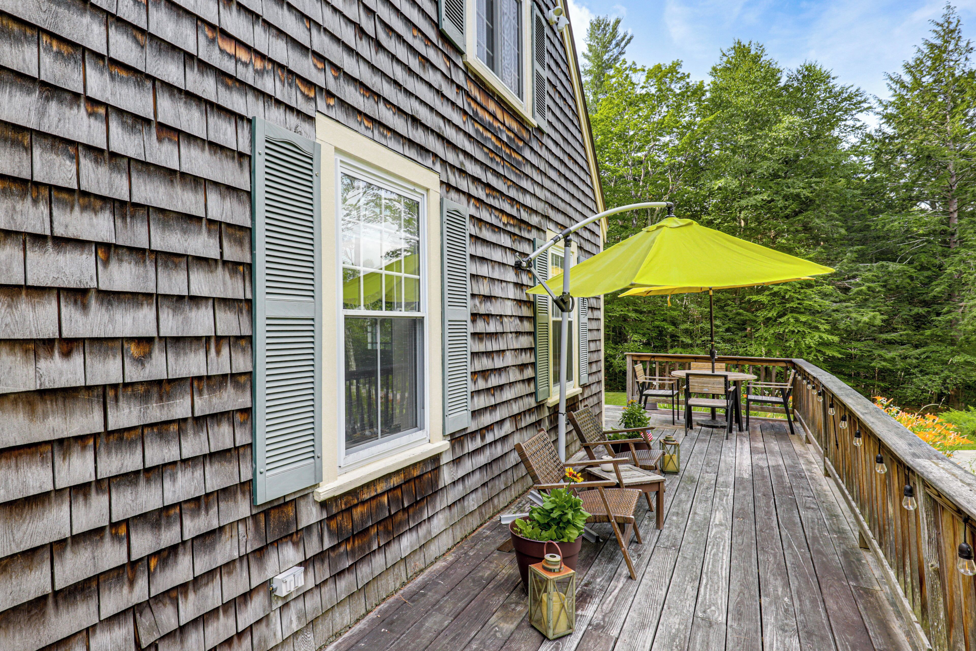 A wooden deck with outdoor furniture, a yellow umbrella, and a potted plant.