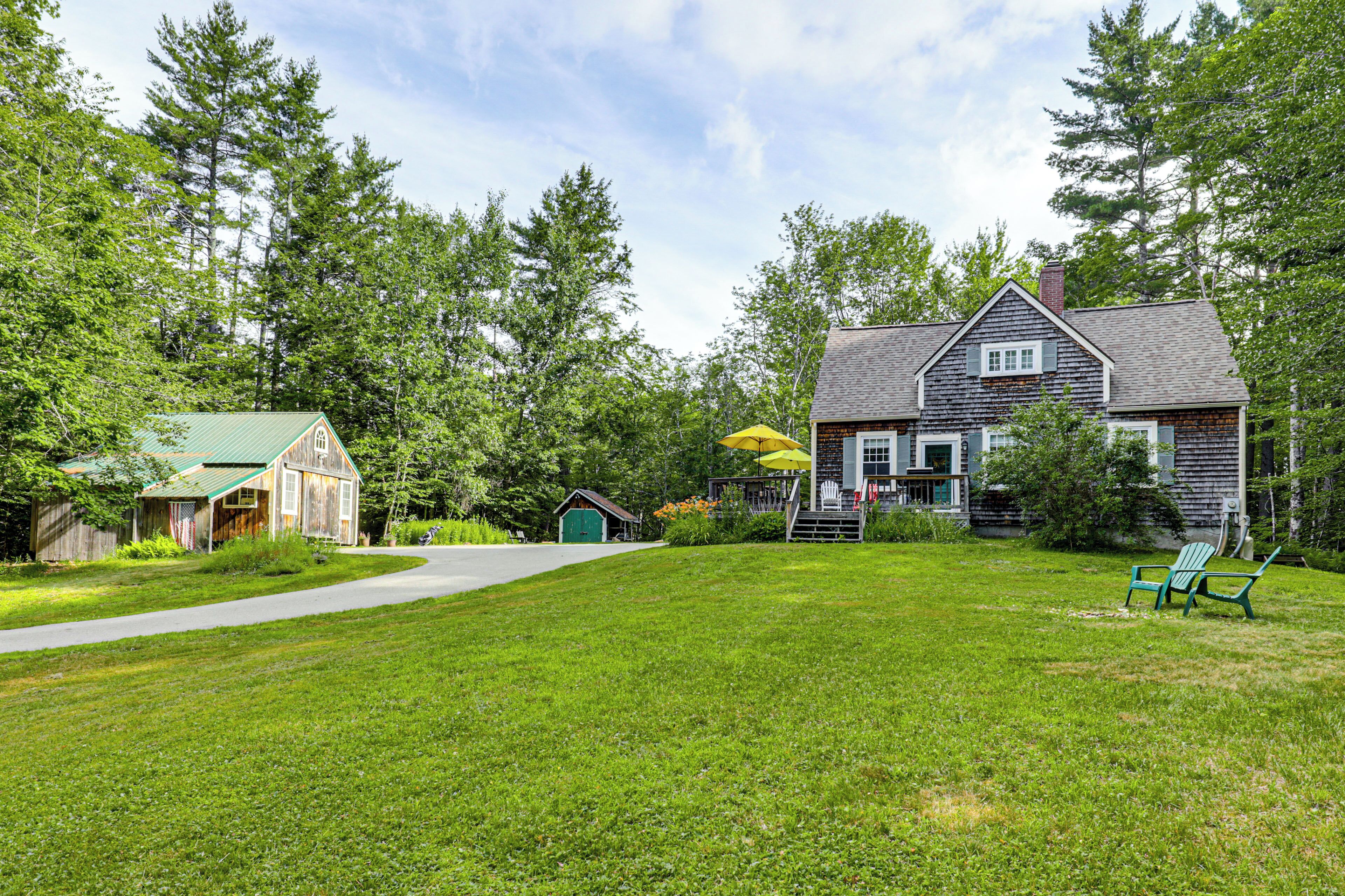 A property with a large lawn, a wooden barn, a main house with a porch, and a small shed.