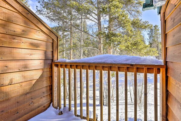 A wooden deck with snow accumulation, surrounded by trees.