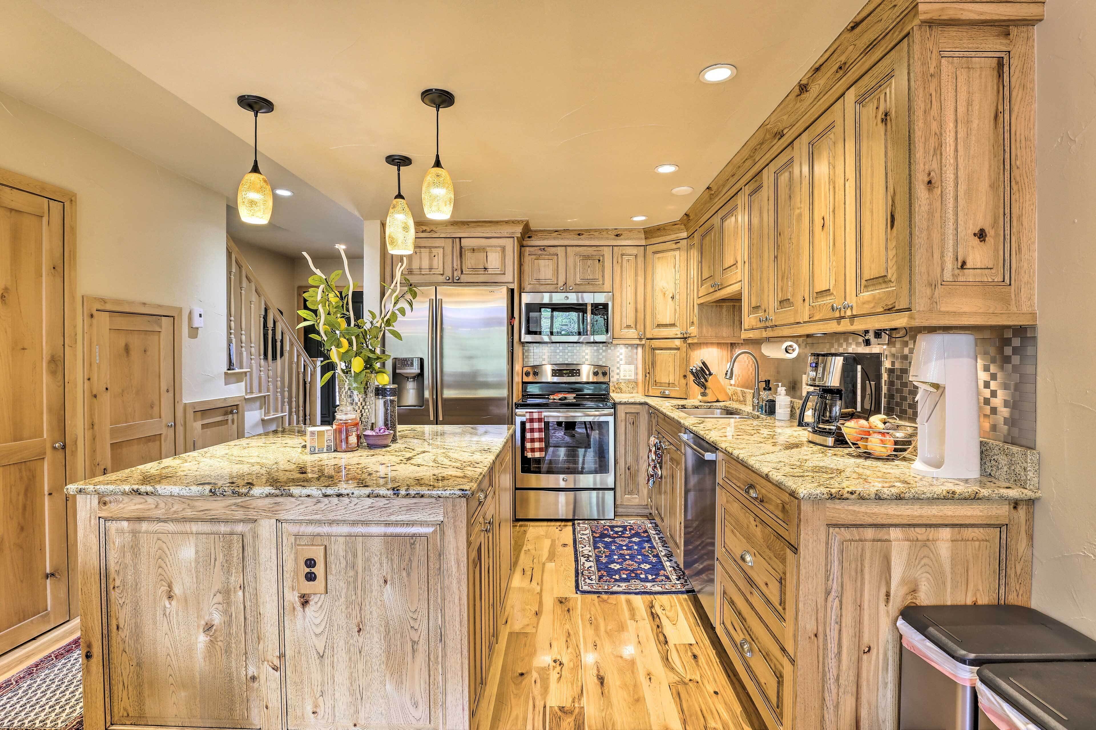 A kitchen with wooden cabinets, granite countertops, stainless steel appliances, and pendant lighting.