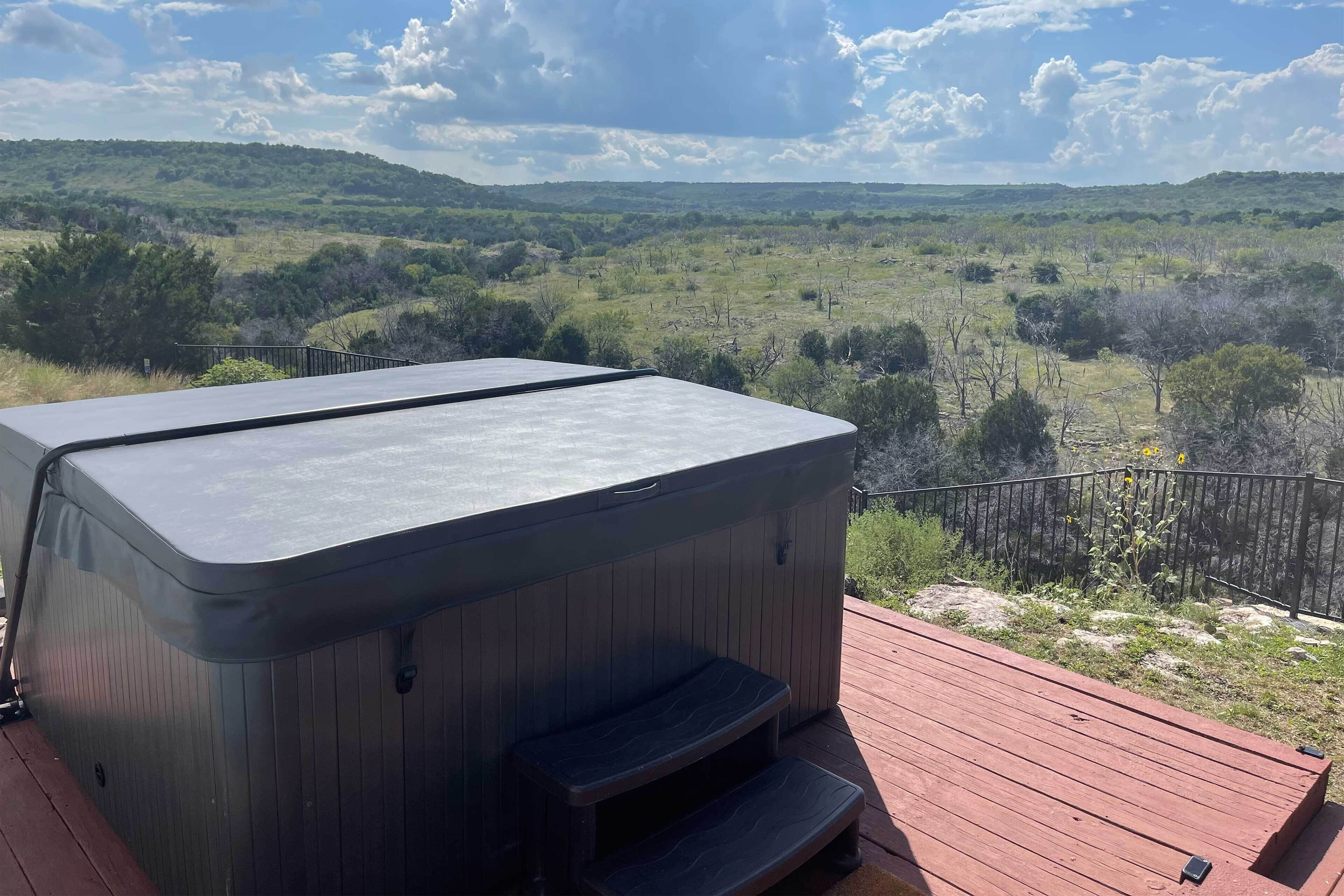 A hot tub on a wooden deck with a view of a grassy landscape.