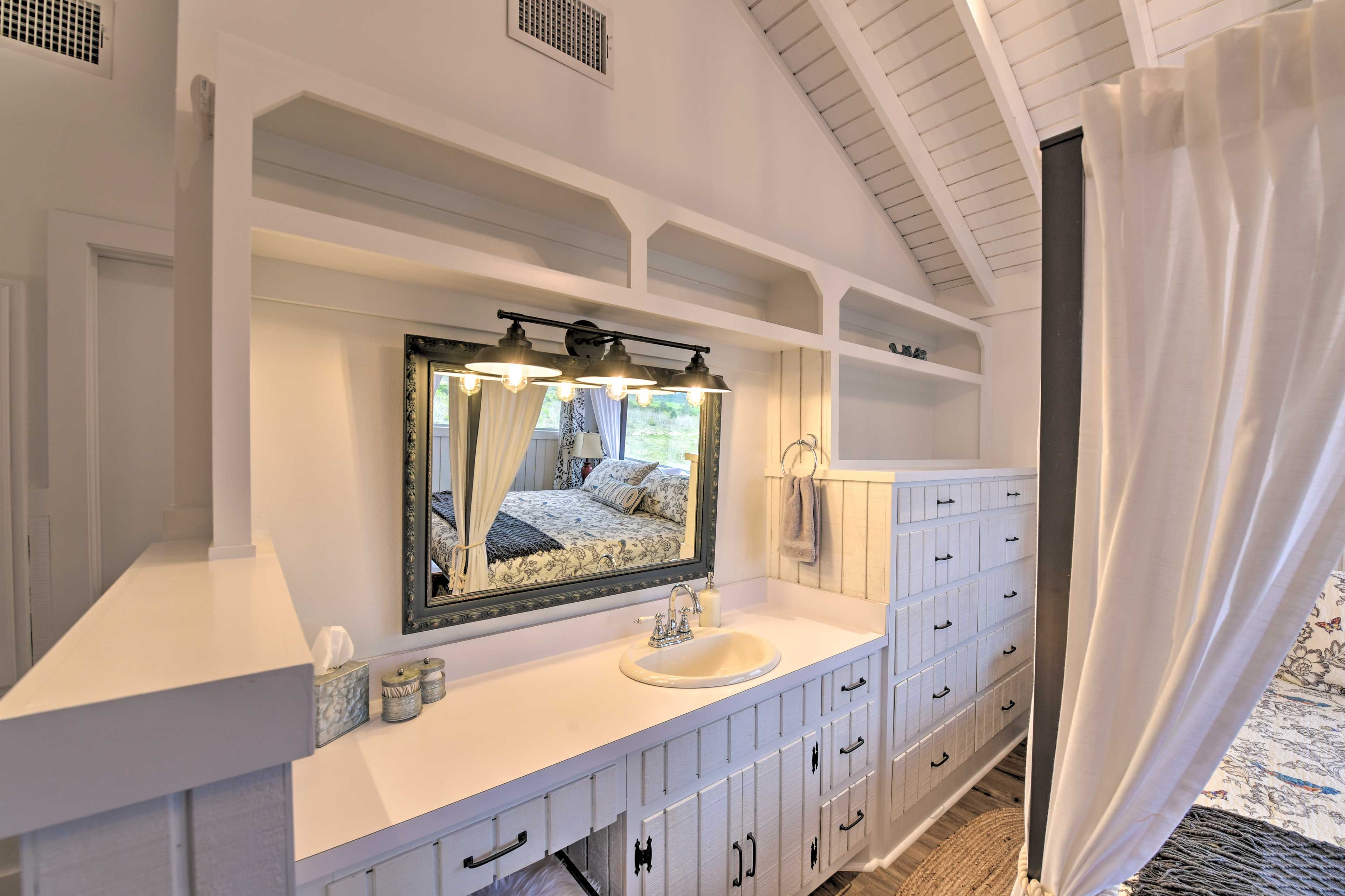 A bathroom with a large mirror, a sink, and a vanity with drawers.