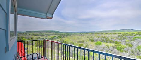 Un balcone con ringhiera in metallo, una panca rossa e vista su un paesaggio verde con alberi e colline.