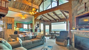 A cozy living room with a fireplace, a large sofa, and a dining area with a view of the ocean. - Lakefront Montague Cottage w/ Deck & Beach! (Montague)