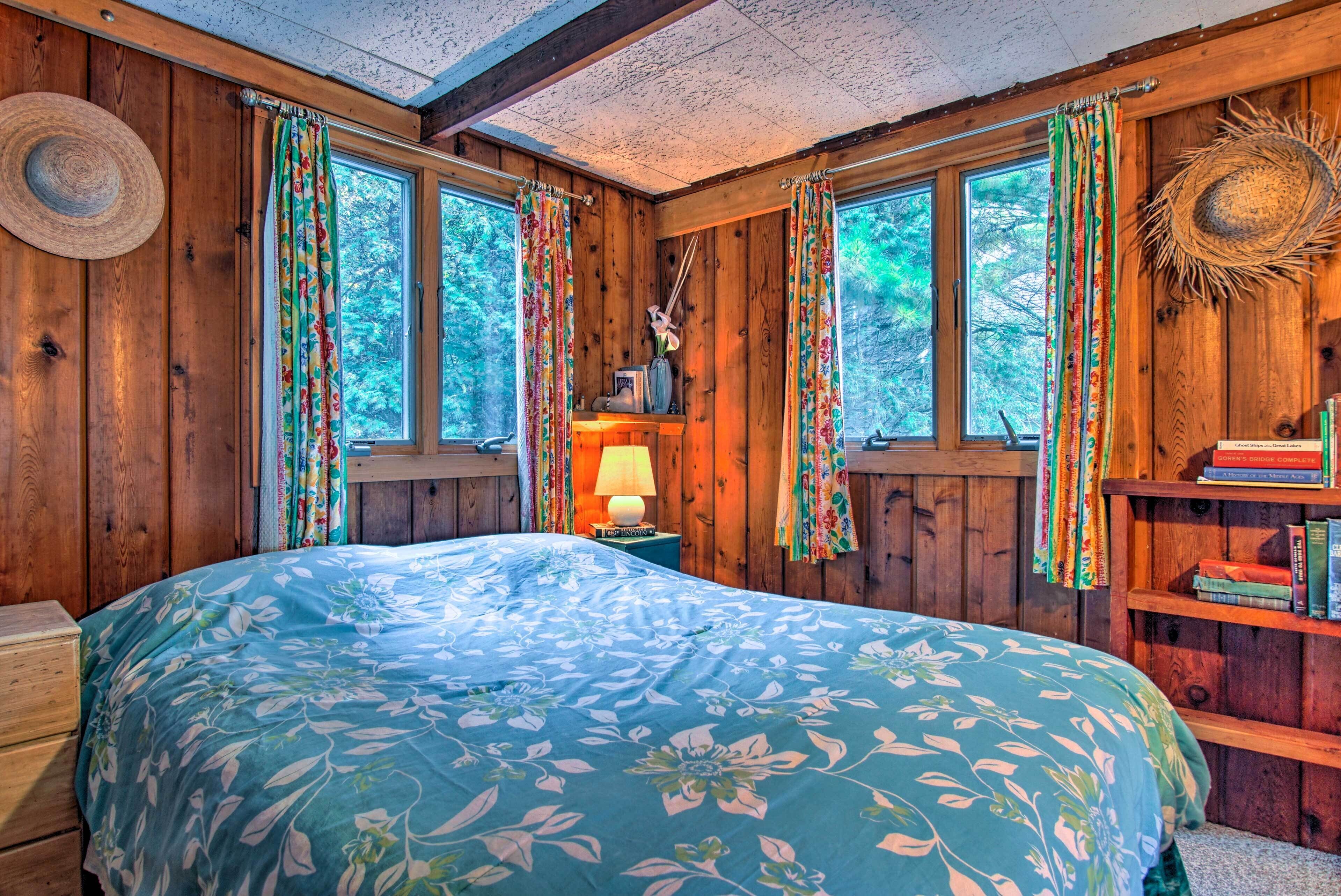 Un dormitorio de cabaña de madera con cama, ventanas y una estantería.
